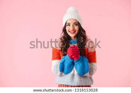Beautiful young smiling woman wearing sweater and a hat standing isolated over pink background