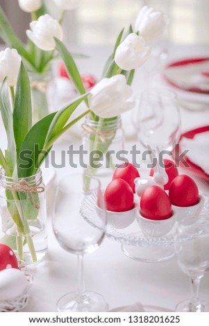 Happy easter. Decor and table setting of the Easter table is a vase with white tulips and dishes of red and white color. Easter colored eggs with white polka dots. Selective focus