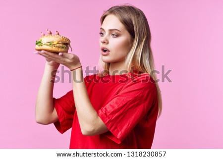 Pretty woman in red t-shirt holding a hamburger in hands Fastfood pink background