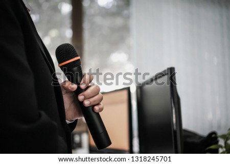 Speaker or businessman hold Microphone for speech or speaking in seminar Conference room, talking for lecture to audience university, Computer monitor desk Background. Business Presentation concept 