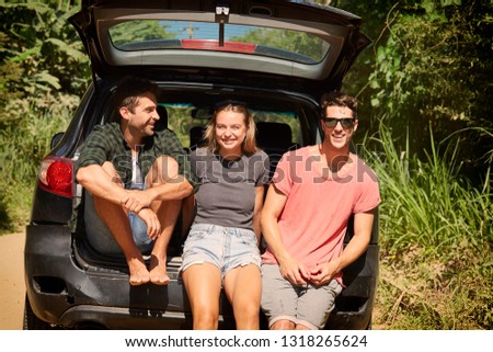 Three road trip friends smiling from trunk of car, portrait