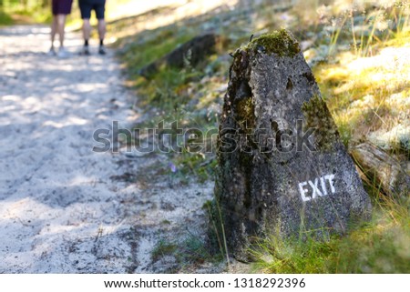 Exit sign on a stone. Two people standing in the background on a path to the beach. In Nida, Lithuania, in curonian spit.