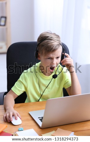 Cute emotional boy playing video game on laptop at home