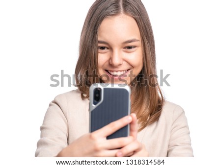 Portrait of beautiful Teen Girl talk to Mobile Phone, isolated on white background. Smiling Child standing and using Cell Phone. Pretty modern Teenager taking Selfie photo on Smartphone.