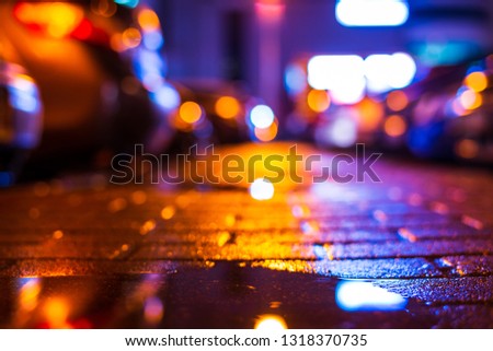 Rainy night in the city. Parking mall with cars. Reflections of shop windows on the wet pavement. Colorful colors. Close up view from the level of the puddle on the pavement.