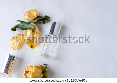 Close up skincare product glass bottle mockup sample styling with dried yellow roses and dried leaves on white fabric texture table top background. Product studio styling shot.