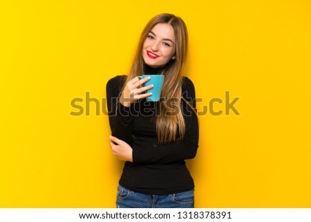 Young pretty woman over yellow background holding a hot cup of coffee