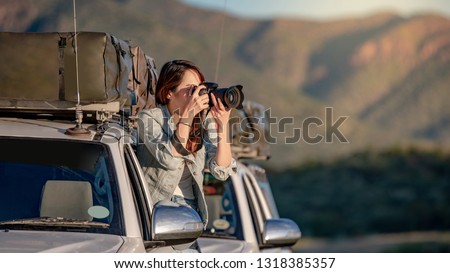 Young Asian woman traveler and photographer sitting on the car window taking photo on road trip in Namibia, Africa. Travel photography concept