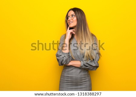 Young woman with glasses over yellow wall thinking an idea while looking up