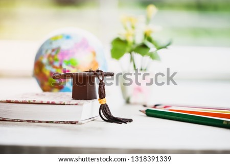 Graduate or Education knowledge learning study abroad concept : Graduation cap on book with blur of Europe earth world globe, with color pencils on wood floor. Work and travel. Back to School