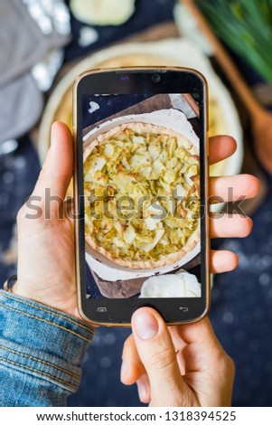 Smartphone food photography. Woman hands take phone food photo. Dinner, tart, veggie pie, table, black dark background. Vegetarian healthy lunch. Blogging or social networks style. Top, above view.