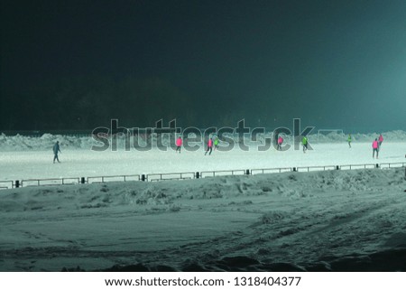 football team plays football in the evening in winter, shining lights and people playing football on the field with snow