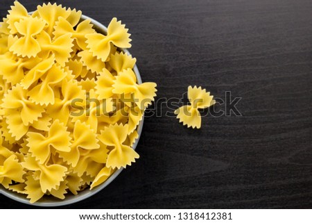 Top view of black background with italian raw farfalle or pasta in grey bowl with copy space