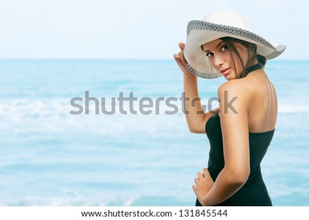 Pretty young woman holding her hat on her head, at the beach