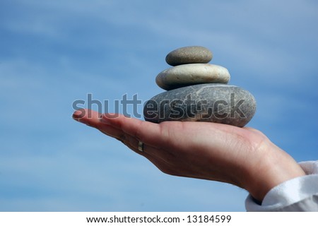 hand balancing stacked stones over blue sky