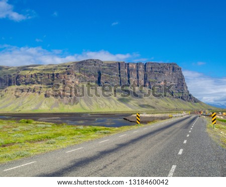 Narrow road segment marked by striped warning signs on a straight asphalt highway under bright blue sky near rocks. Iceland landscape, summer season. Signs with diagonal black and yellow lines.