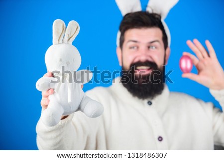 Easter fun. Bearded man with bunny toy and Easter egg. Hipster with long rabbit ears holding egg laying hare. Easter bunny delivering colored eggs. Celebration of spring time holiday.