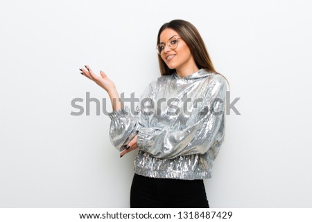 Young woman with glasses over white wall extending hands to the side for inviting to come