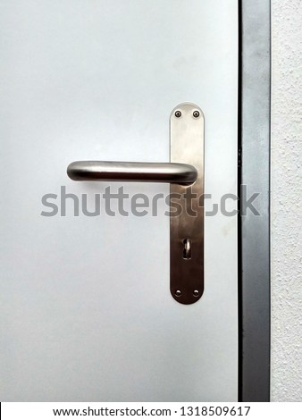 Metallic door knob, handle with key on white door close up.