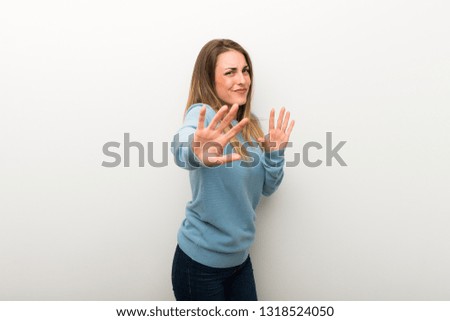 Blonde woman on isolated white background is a little bit nervous and scared stretching hands to the front