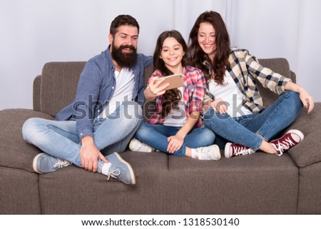 Capture happy moments. Family spend weekend together. Use smartphone for selfie. Friendly family having fun together. Mom dad and daughter relaxing on couch. Family posing for photo. Family selfie.