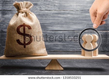 Magnifying glass is looking at the people and a money bag with a dollar sign on the scales. attracting investment, business cooperation, crowdfunding and startup. the cost of specialists and workers