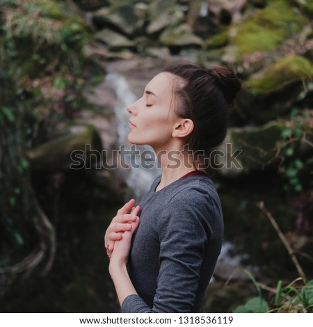 Young woman practicing breathing yoga pranayama outdoors in moss forest on background of waterfall. Unity with nature concept Royalty-Free Stock Photo #1318536119