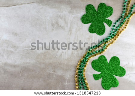 Two shamrocks on right hand side on tan stone tile background.  With gold and green beads.  Copy space.