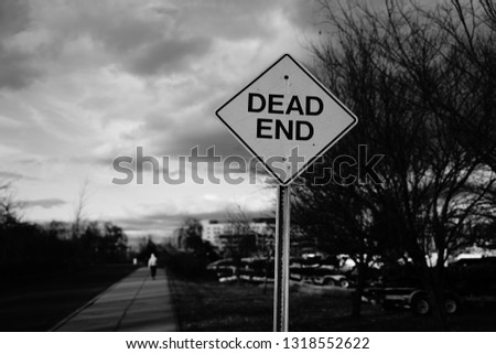 Sign dead end with a man going away behind it b&w