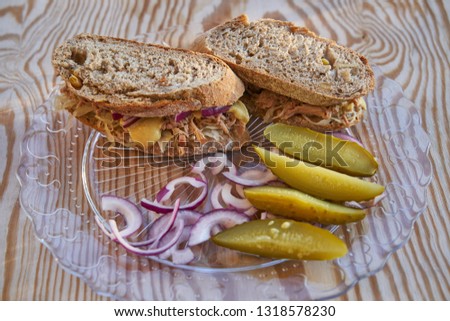  Close up Picture of the sandwich made from whole grain bread, pulled pork, sour gabbage, onion and mustard served with pickled cucumbers, light dish or modern street food                             