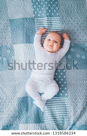 Adorable lovely newborn male baby with blue eyes lifestyle indoor portrait from above. Cute child with hands apart lying on back in pijama on bed at home. Little child with emotional face rest on sofa
