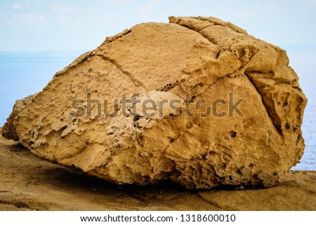 The picture shows a large yellow stone in close-up. The stone is painted on the land of Malta in the town of blue groto. Behind the stone you can see how the sky and the sea connect in the distance
