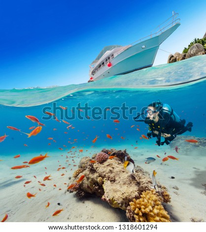 Under and above water surface view of woman diver. Underwater fauna and flora, marine life and exotic island with anchoring yacht on background