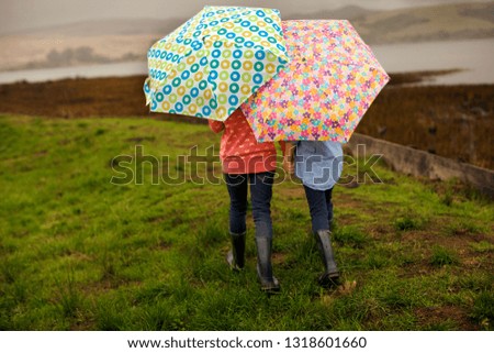 Two sisters walking hand in hand while holding umbrellas.