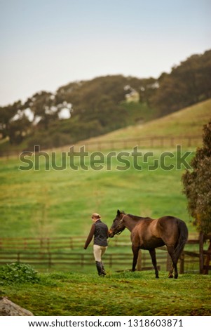 Mid adult woman leading her horse in a grassy pasture.