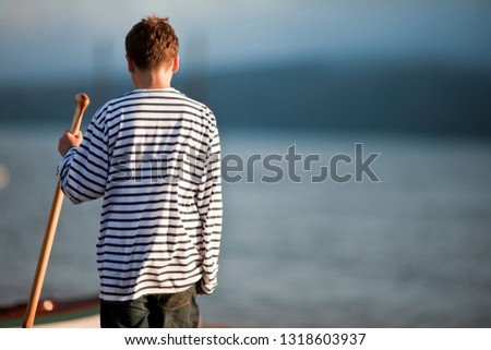 Rear view of boy holding oar at water's edge.