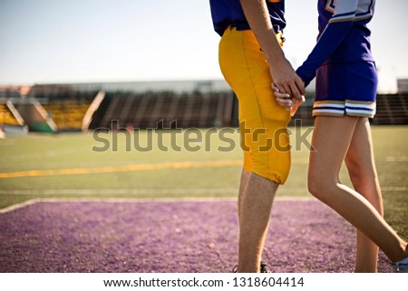 Football player and cheerleader holding hands on football field