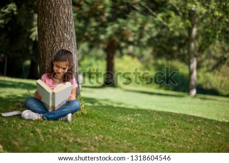 Happy young girl reading a book under a tree.