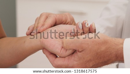 Extreme close up on doctor taking radial pulse on wrist of female patient. Woman with bejeweled rhinestone nail art having heart rate measured by medical professional