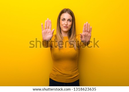 Young woman on yellow background making stop gesture for disappointed with an opinion