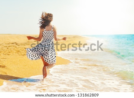 Young happy woman running barefoot  on the beach back to camera Royalty-Free Stock Photo #131862809