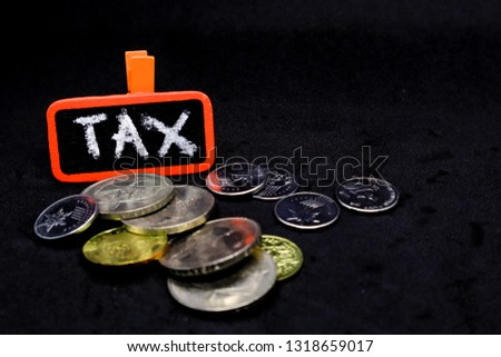 The word “TAX” written using chalk on a piece pf board on isolated black backgrounds and coins around it.