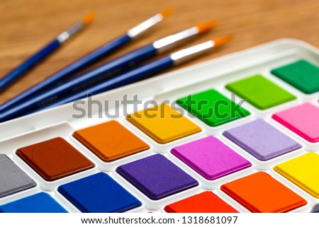 Set of solid watercolors and paintbrush on wooden table background