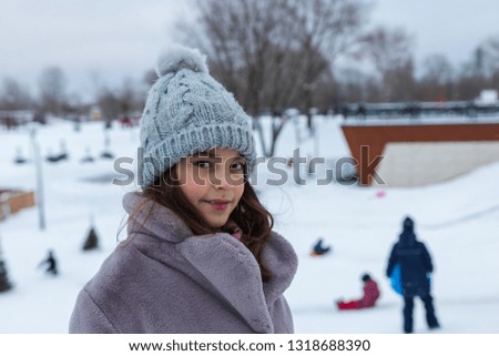 background, children sledding. portrait, beautiful girl in a gray hat and a fur coat on a snowy hill.