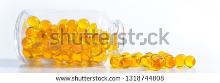 Yellow capsules scattered from a glass jar on a white background.