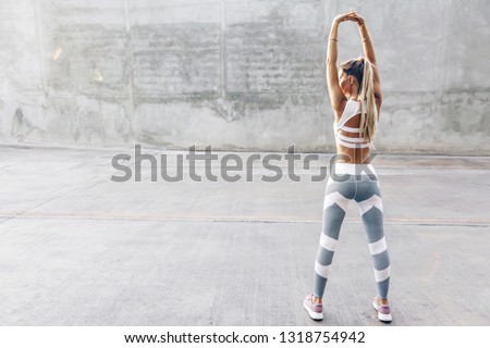 Fitness woman in sportswear doing stretching exercise on the city street over gray concrete background. Outdoor sports clothing and shoes, urban style. Royalty-Free Stock Photo #1318754942
