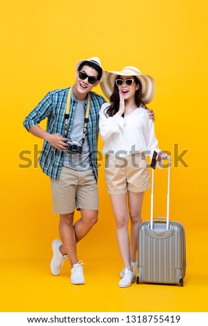 Happy excited young Asian couple tourists in colorful yellow background