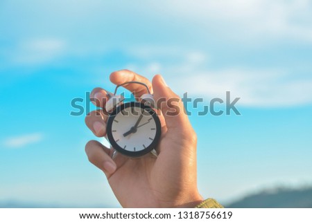 Small circle alarm clock at eight o'clock in man's hand,lift up in clear blue sky and soft cloud with mountain background.Copy space for texts.Concept for time or chance keeping.
