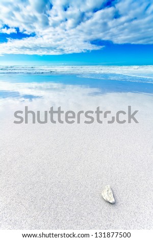 Ocean seascape. White rock or pebble in a white sandy beach under blue and cloudy sky in a bad weather. Waves on background.
