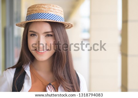 Happy Asian Chinese traveler smiling; portrait of Chinese Asian tourist with hat and backpack looking in European style building architecture; holiday, vacation, travel, tourism concept